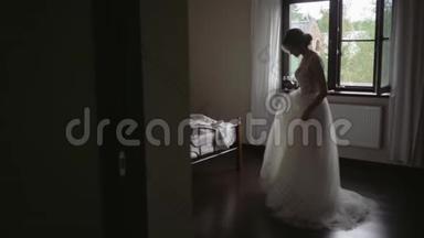 美丽的新娘在卧室里欣赏她的婚纱。 穿着婚纱的美丽年轻新娘